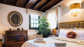 A bedroom with a large bed, a wooden dresser, a mirror, a potted plant, and a window with curtains. - Ktima Zotos _ Luxury Exotic Cottage 1 (Volos - Pelion) (SOUTRALI AGRIA)