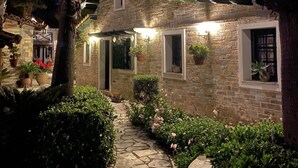 A stone building with a tiled roof, illuminated by string lights, surrounded by greenery and a stone pathway. - Ktima Zotos _ Luxury Exotic Cottage 1 (Volos - Pelion) (SOUTRALI AGRIA)