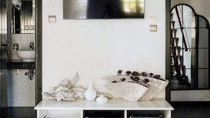 A modern living room with a large flat-screen TV mounted on the wall, a white console table with decorative items, and a mirror reflecting the room. - Ktima Zotos _ Luxury Exotic Cottage 1 (Volos - Pelion) (SOUTRALI AGRIA)