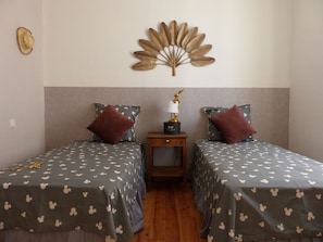 Une chambre avec deux lits simples, chacun agrémenté d’une couvre-lit sur le thème de Mickey Mouse, une petite table de chevet avec une lampe et un élément décoratif mural au-dessus des lits.