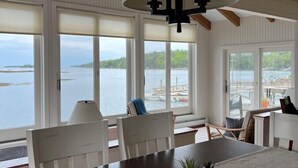 A dining area with a large table, chairs, and a hanging light fixture. - Linekin Lodge | Oceanfront | 3BDR| Deep Water Dock| Beach (Boothbay Harbor)