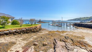 A coastal property with a stone wall, grassy area, and a dock extending into the water. - Linekin Lodge | Oceanfront | 3BDR| Deep Water Dock| Beach (Boothbay Harbor)