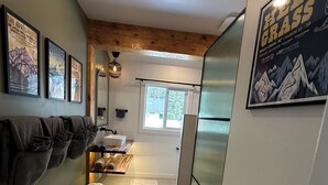 A narrow hallway with a wooden ceiling, a window, and a bathroom with a sink and towel rack. - Bearvalley Guesthouse (Stewart)