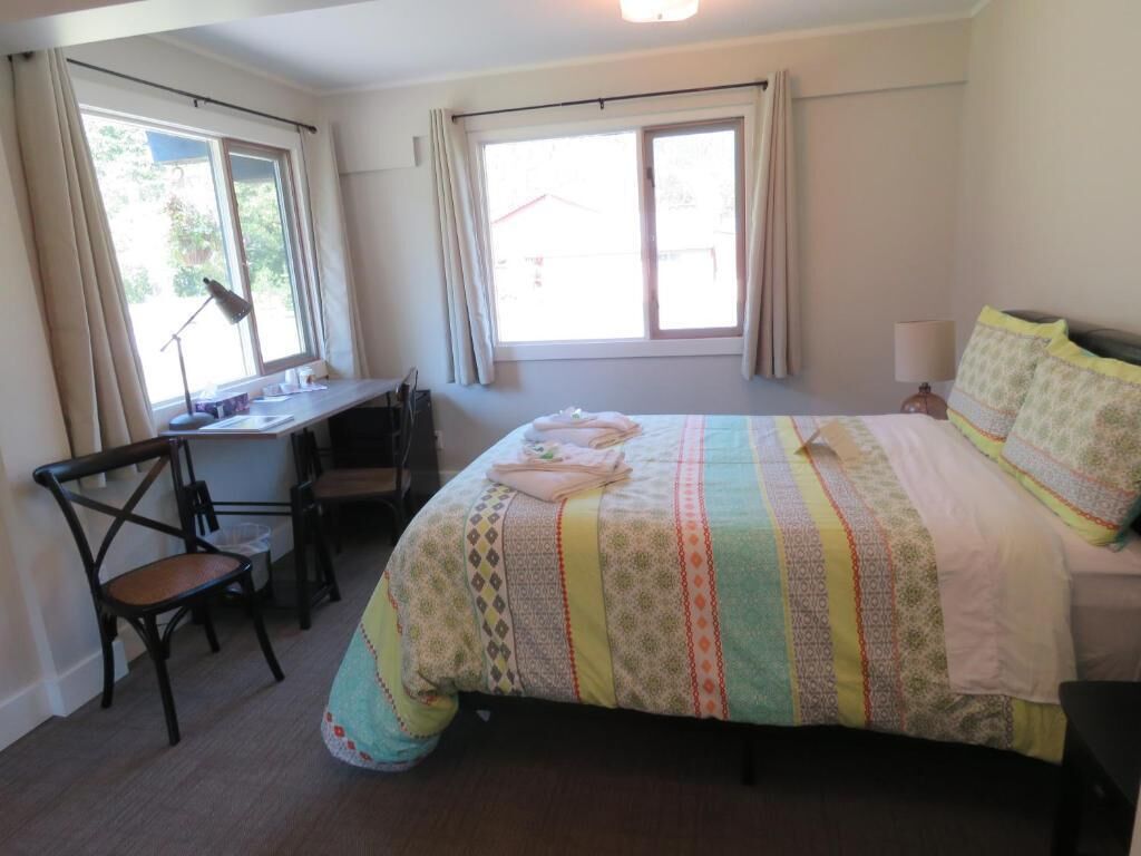 A bedroom with a bed, a desk, and two windows.