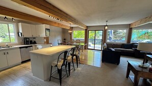 A modern kitchen with a central island, wooden beams, and a dining area with a view of the outdoors. - Bearvalley Guesthouse (Stewart)
