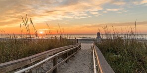 A wooden boardwalk leading to a beach with a signpost in the distance.