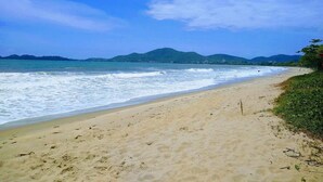 A beach with a sandy shore, waves, and distant green hills. - Nautilus Paraíso Tropical - Vista ao Mar (Penha)