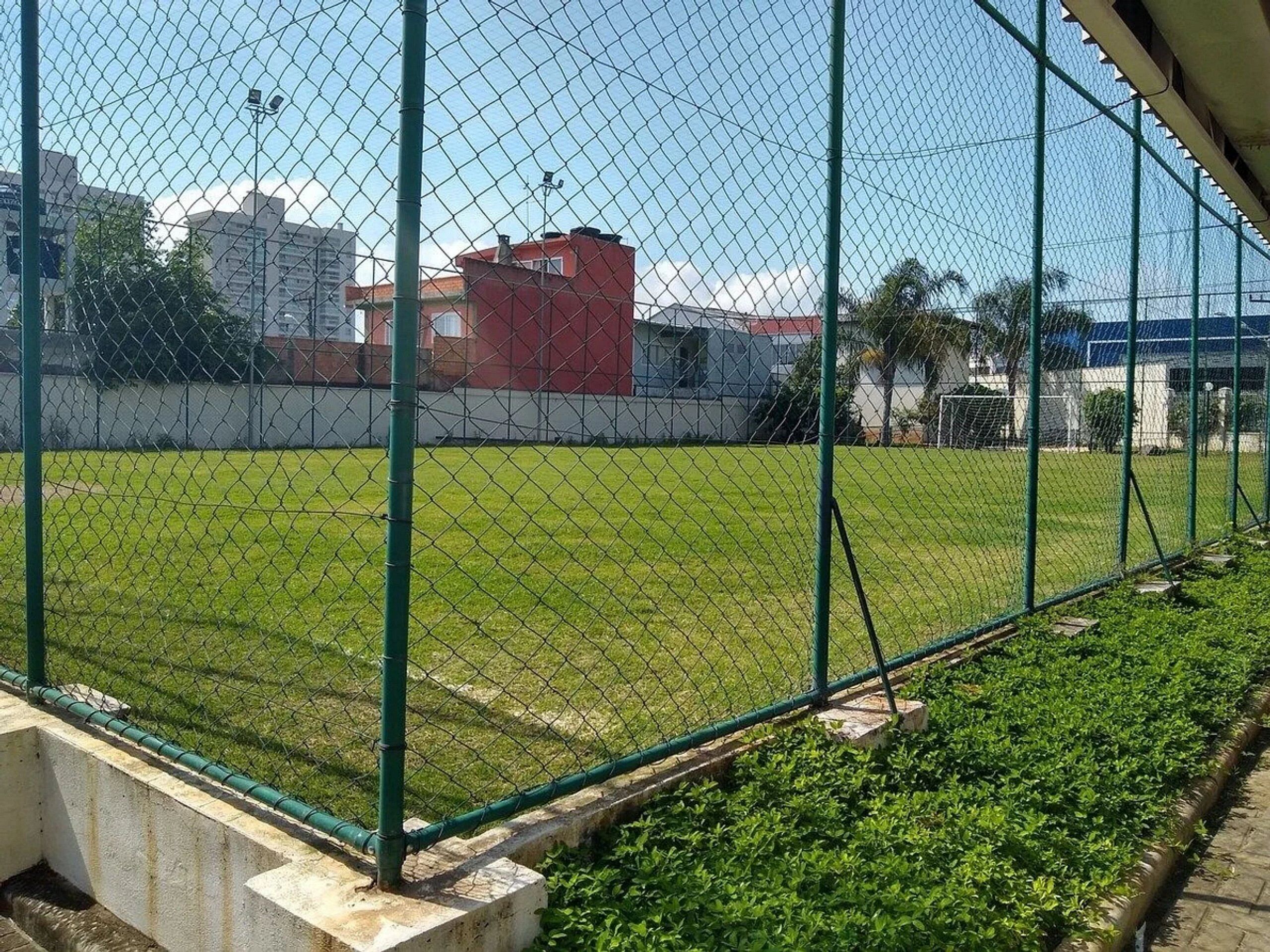 Uma cerca de arame envolvendo um campo gramado com edifícios ao fundo.