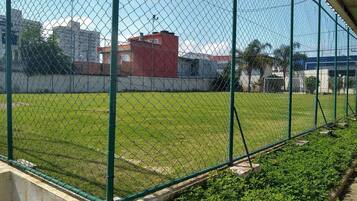 Uma cerca de arame envolvendo um campo gramado com edifícios ao fundo.