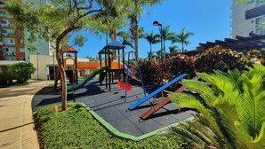 A playground with slides and climbing structures, surrounded by greenery and palm trees. - Nautilus Paraíso Tropical - Vista ao Mar (Penha)