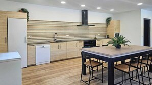 A modern kitchen with wooden cabinets, a built-in oven, and a dining area with a table and chairs. - Casitas Cueva del Gato Benaoján by Ruralidays (Málaga)