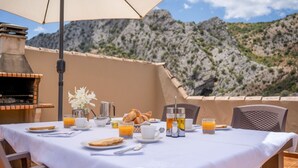 A table set for breakfast with croissants, orange juice, and coffee, overlooking a mountainous landscape. - Casitas Cueva del Gato Benaoján by Ruralidays (Málaga)