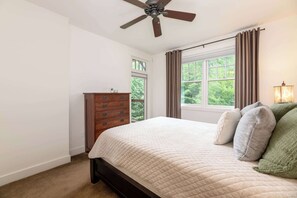 A bedroom with a bed, a dresser, a ceiling fan, a window with curtains, and a lamp.
