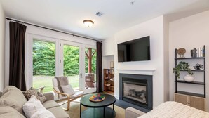 A living room with a fireplace, a television, a bookshelf, and a view of the outdoors. - Riverfront Condo w/ Hot Tub | River Swimming Spot! (Lincoln)