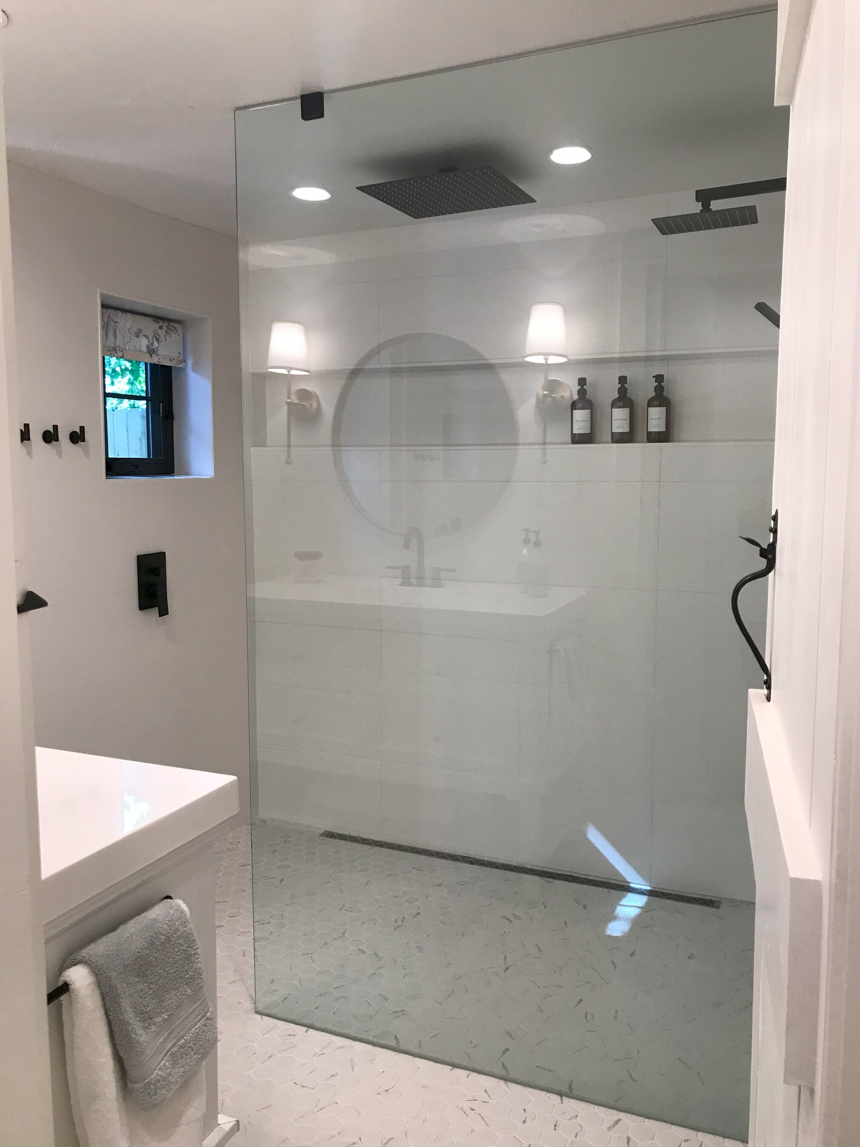 Un baño moderno con cabina de ducha de vidrio, tocador con espejo y una ventana pequeña.