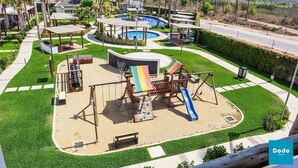 Un parque infantil con tobogán y columpios, una piscina y una carretera al fondo.