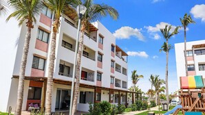 Un hotel de varios pisos con balcones, palmeras y un tobogán para niños.