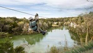 Experience the rush of zip-lining over a serene body of water surrounded by lush vegetation.