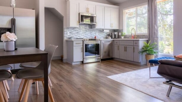 A modern kitchen with white cabinets, stainless steel appliances, and a large window providing natural light.