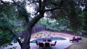 A backyard with a hot tub, a dining table with chairs, and a wooden fence.