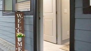 A house entrance with a 'WELCOME' sign, a door, and a blue mat.