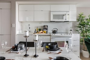 Una cocina moderna con armarios blancos, microondas, estufa y un comedor con copas de vino y cubiertos.