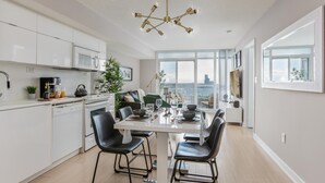 A modern kitchen with white cabinets, a dining area with a glass table, black chairs, and a city view through large windows.