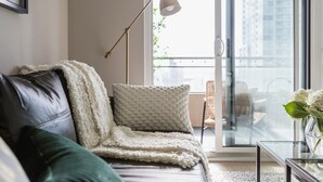 A modern living room with a sofa, a floor lamp, and a view of a balcony with outdoor furniture.