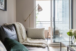 Uma sala de estar moderna com um sofá, um abajur e vista para uma varanda com mobiliário de exterior.