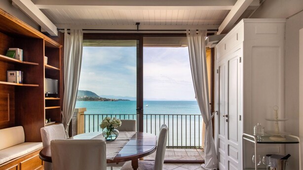 A balcony with a view of the sea, a dining table with chairs, a sofa, and a bookshelf. - Meravigghia Apartment by Wonderful Italy (Cefalù)