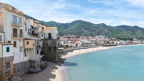A coastal town with buildings along the beach, a clear blue sea, and a hilly backdrop. - Meravigghia Apartment by Wonderful Italy (Cefalù)