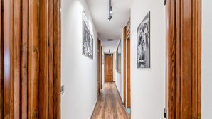 Un pasillo con pisos de madera y puertas que conduce a una habitación con cama y ventana.