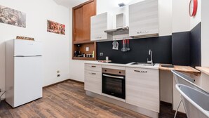 Cocina compacta con horno integrado, refrigerador y un mueble de madera.