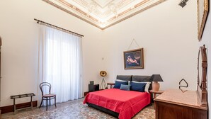 Un dormitorio con suelo estampado, una cama con colcha roja, una silla, un escritorio y una lámpara.
