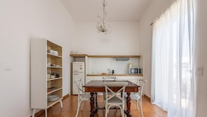 A dining area with a wooden table and white chairs, a white cabinet with shelves, a microwave, and a refrigerator.