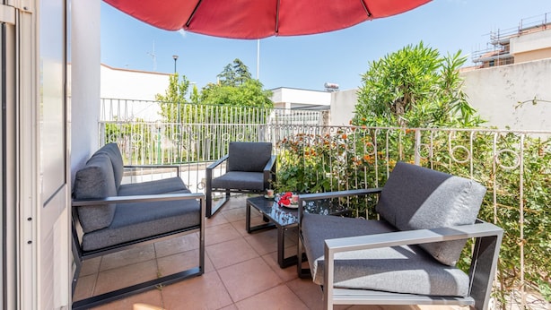 A balcony with outdoor furniture, a red umbrella, and a view of the surrounding area.