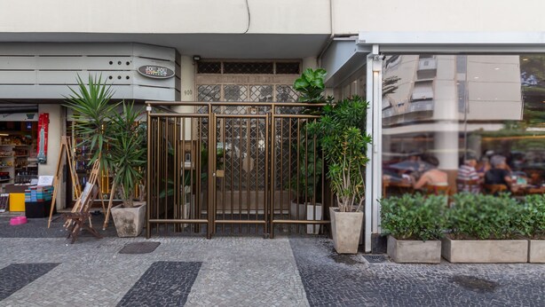 A storefront with a metal gate, potted plants, and a tiled pavement. - 5 Minutes From Leblon Beach Ap102 (Rio de Janeiro)