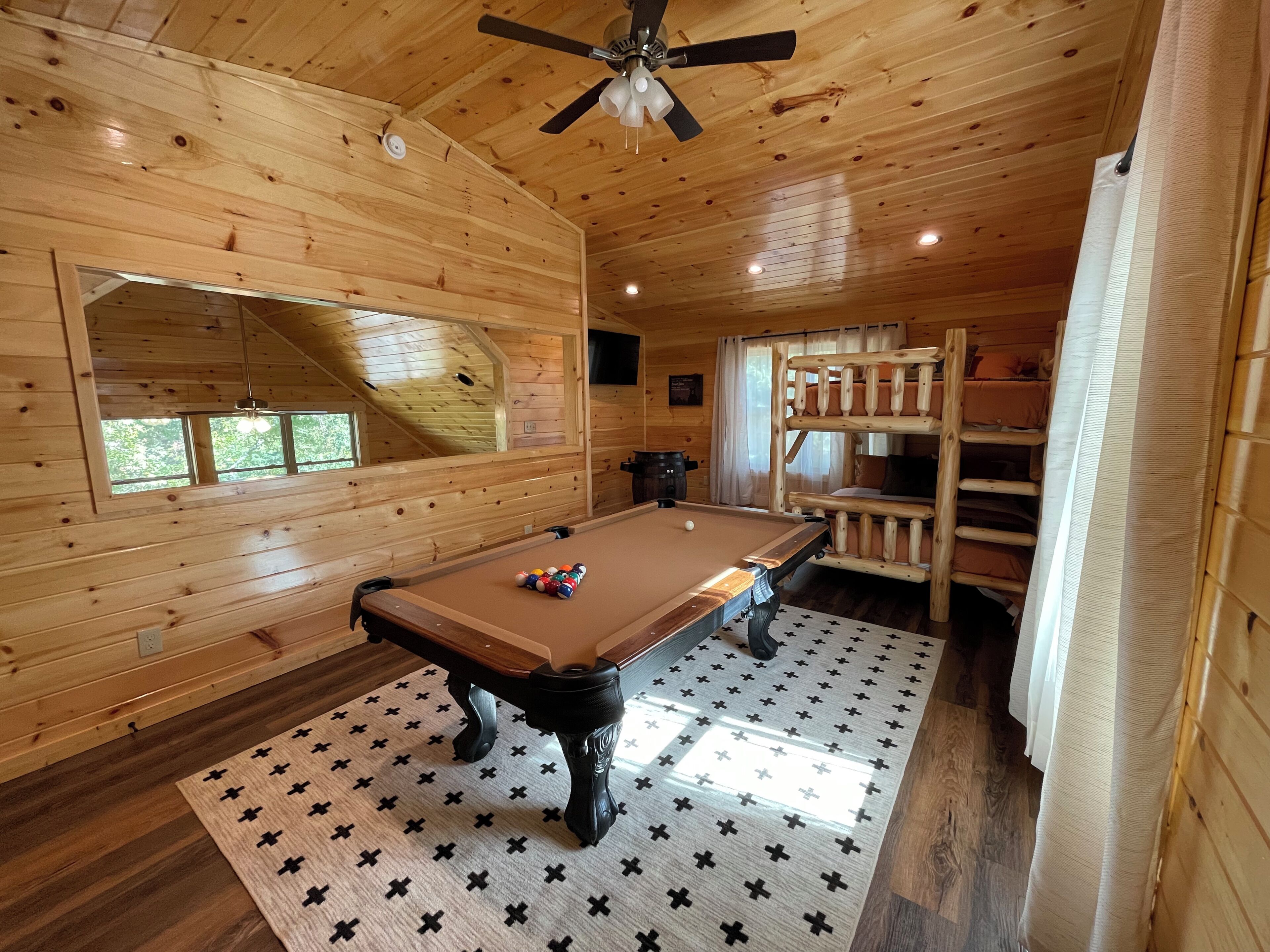 Une cabane en bois avec une table de billard, des lits superposés et un ventilateur de plafond.