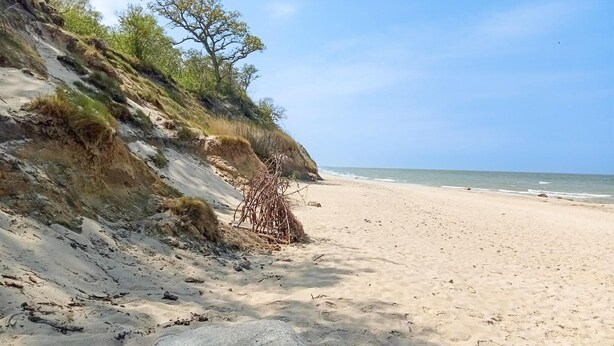 Ein sandiger Strand mit einer felsigen Klippe und spärlicher Vegetation.