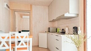 Eine kompakte Küche mit weißen Schränken, einem kleinen Kühlschrank und einem Essbereich mit weißen Stühlen und einem Tisch.