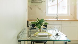 Une cuisine moderne avec une table à manger en verre, des meubles blancs et une fenêtre donnant sur l’extérieur.