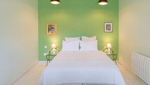 Un lit bien fait dans une pièce aux murs verts, avec deux lampes de chevet et des tableaux encadrés accrochés au mur.