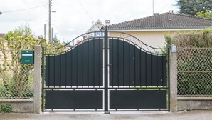 Une entrée fermée par un portail en métal et une boîte aux lettres verte située sur le côté gauche.