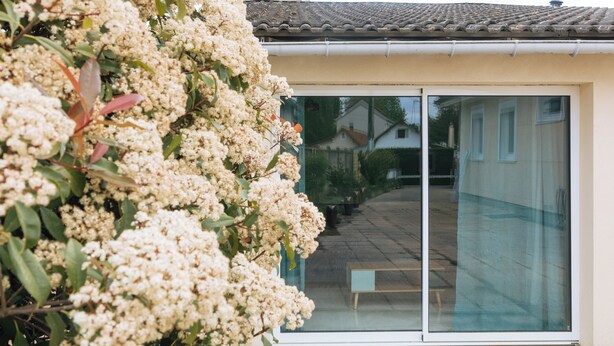 Une maison avec un toit en tuiles, une porte-fenêtre coulissante et un banc à l’extérieur.