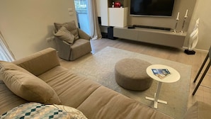 Ett modernt vardagsrum med en beige soffa, ett litet runt bord, en platt-TV och en bokhylla.