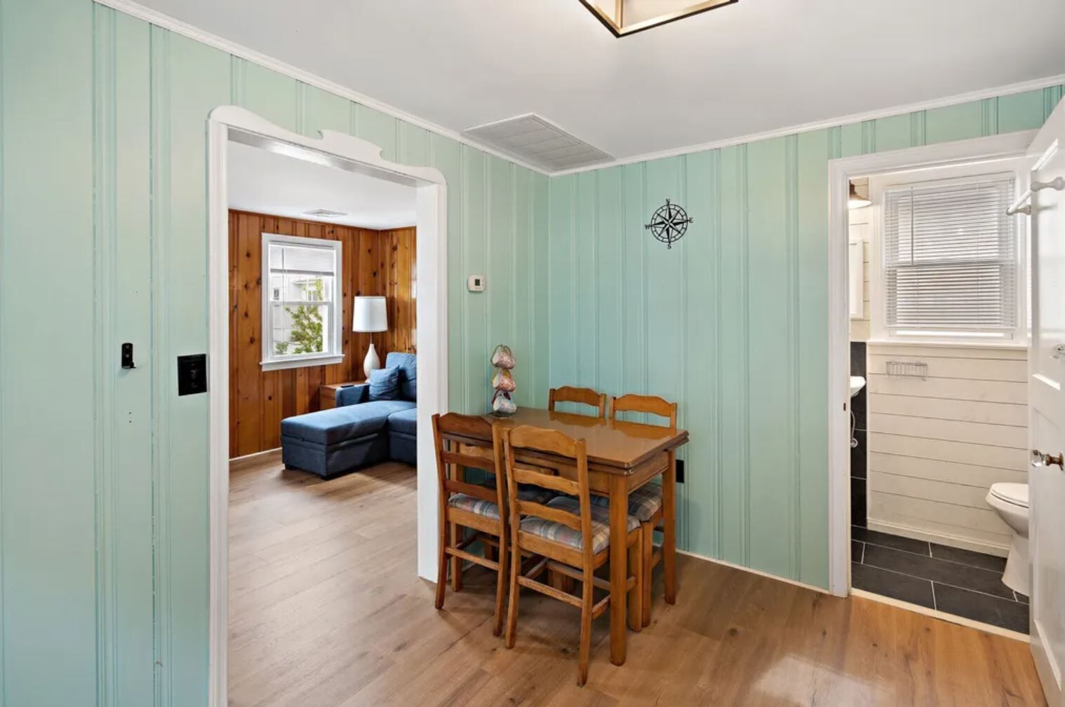 A room with a wooden dining table and chairs, a blue sofa, and a window with blinds.