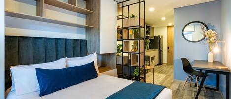 A modern hotel room with a large bed, built-in shelving, a desk, and a dining area.