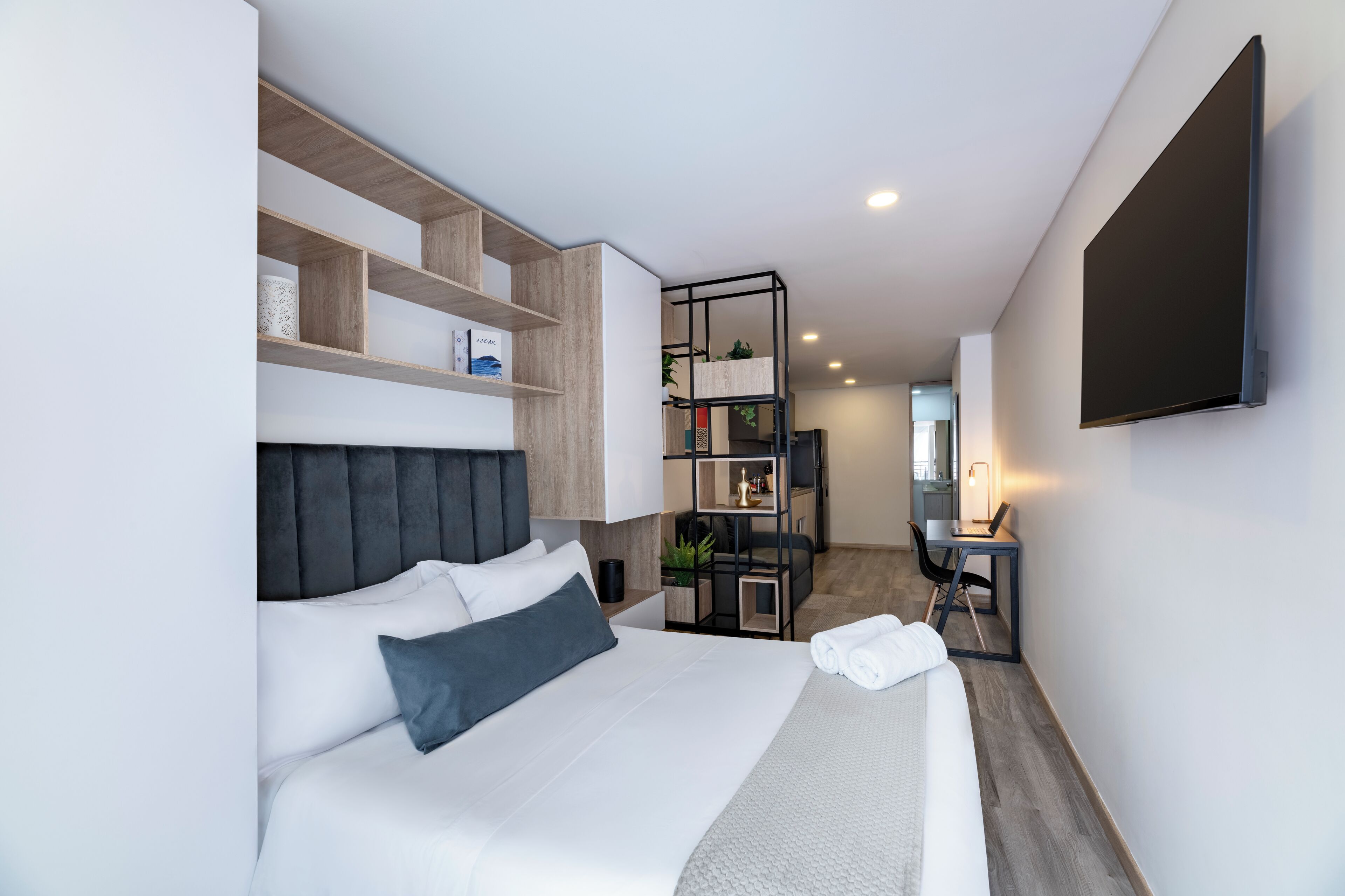 A modern hotel room with a large bed, built-in shelving, a desk, and a flat-screen TV.