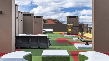 Terraza en la azotea con mobiliario exterior, equipo de ejercicios y vistas a la ciudad.