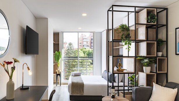 A modern hotel room with a bed, a seating area with a table, a bookshelf, and a TV mounted on the wall. -  Cabrera 85-12 by Jalo (Bogotá)